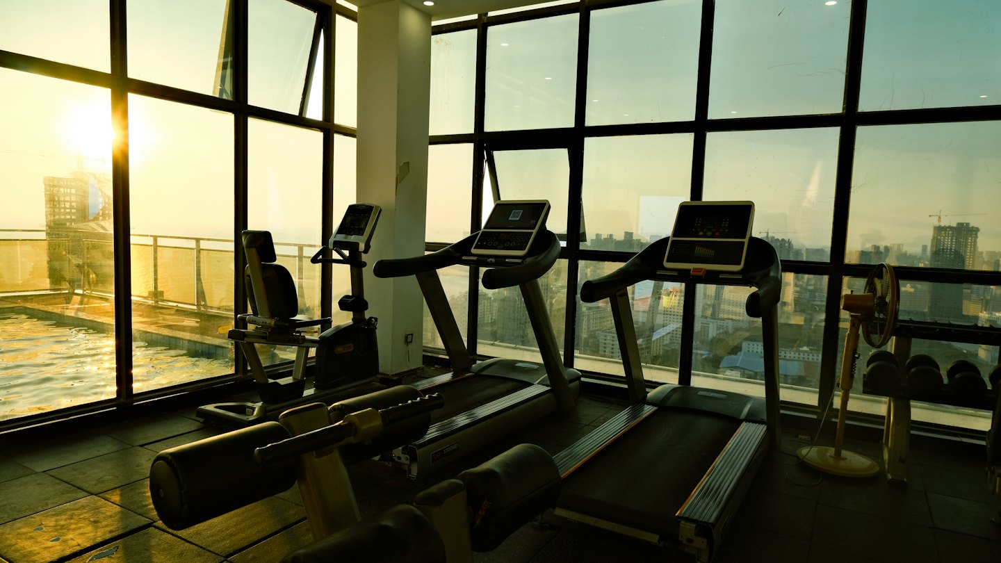 Gimnasio con cintas de correr y bicicleta junto a una ventana con vistas al atardecer.