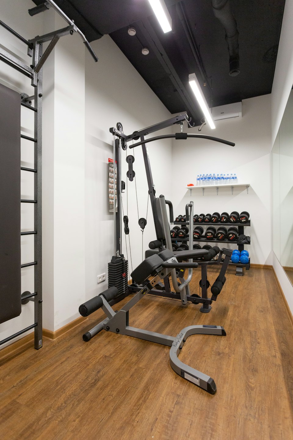 Gimnasio privado vacío con máquina multiestación, mancuernas y pesas rusas.