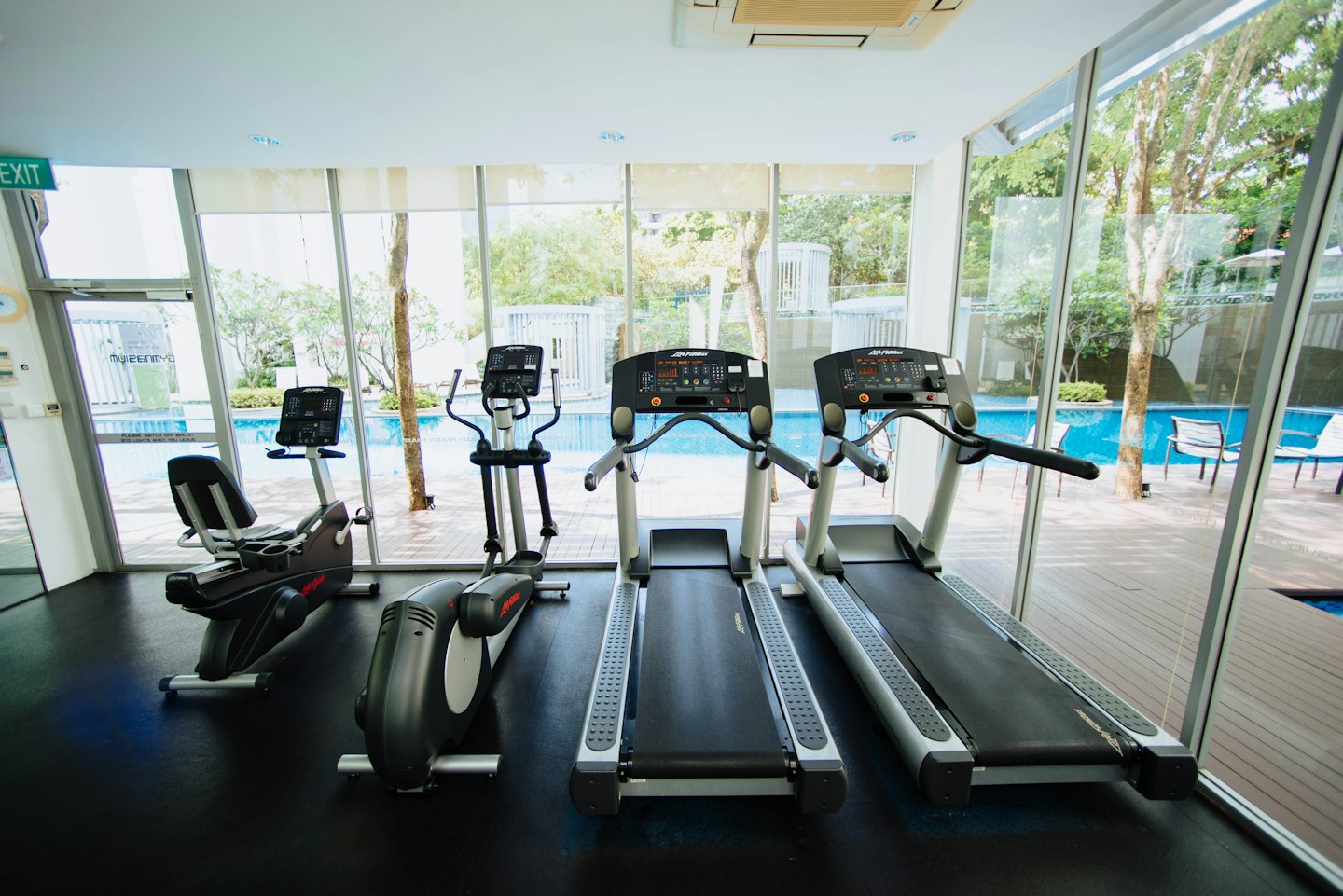 Equipo de gimnasio moderno frente a grandes ventanales con vista a la piscina.