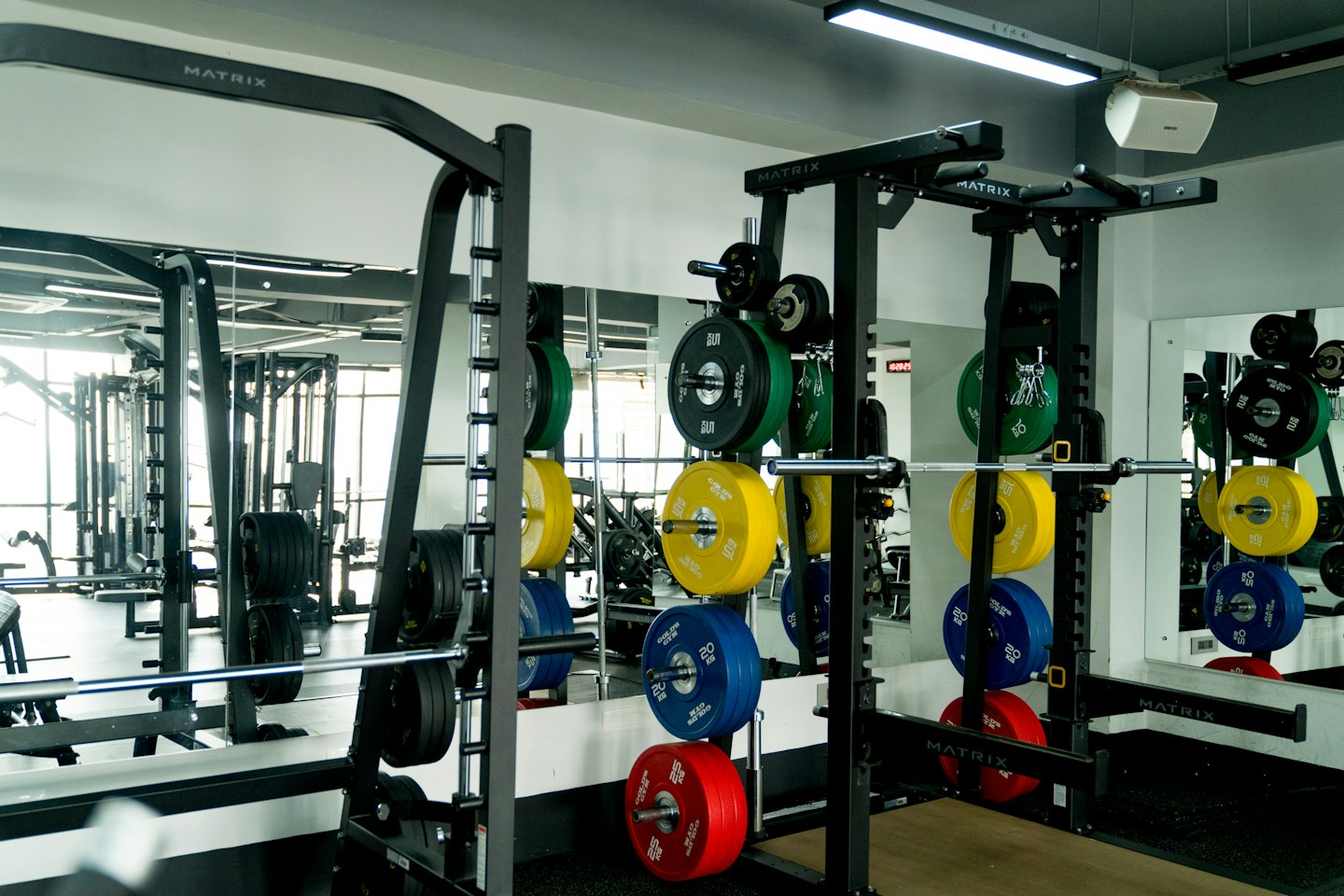 Interior de gimnasio moderno con máquinas de pesas y discos de colores sobre suelo de goma.