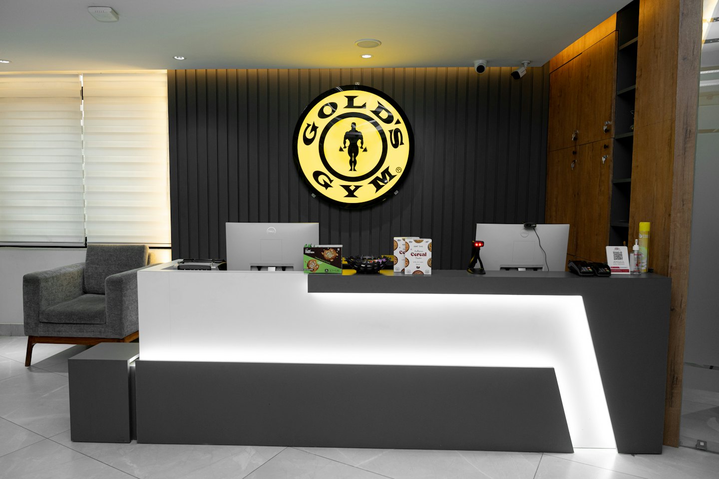 Mostrador de recepción de gimnasio moderno con monitores de computadora y el logo de Gold's Gym.